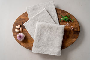 
                  
                    Load image into Gallery viewer, pale sandy set of 3 linen tea towels on the oak wood cutting board
                  
                